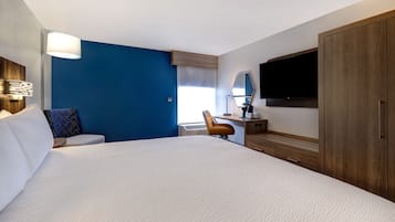 Una habitación de hotel con una cama grande, un escritorio con silla, un televisor y un armario.