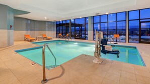 An indoor swimming pool with clear glass walls, multiple lounge chairs, and a lifeguard stand. - Holiday Inn Express & Suites Central Omaha by IHG (Omaha)