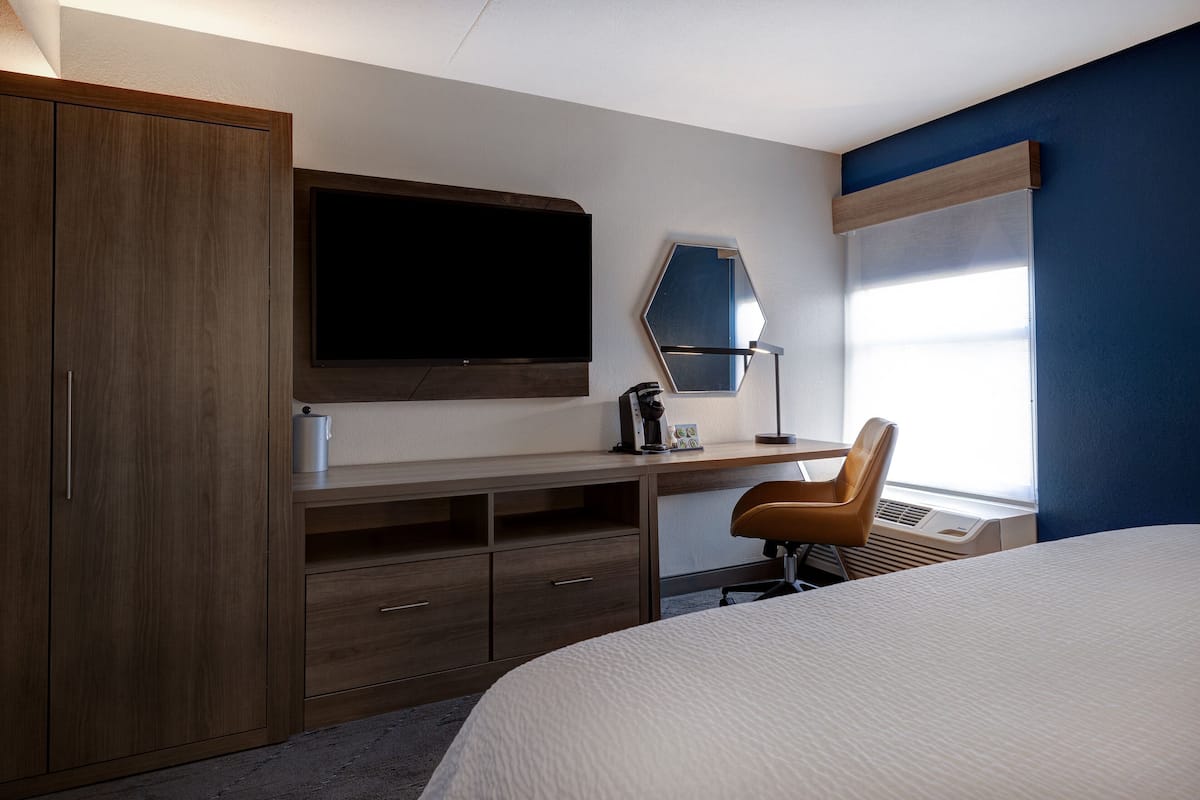 A hotel room with a bed, a desk, a chair, a TV, and a window with blinds.