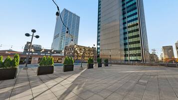 A spacious plaza with modern buildings, street lamps, and potted plants.