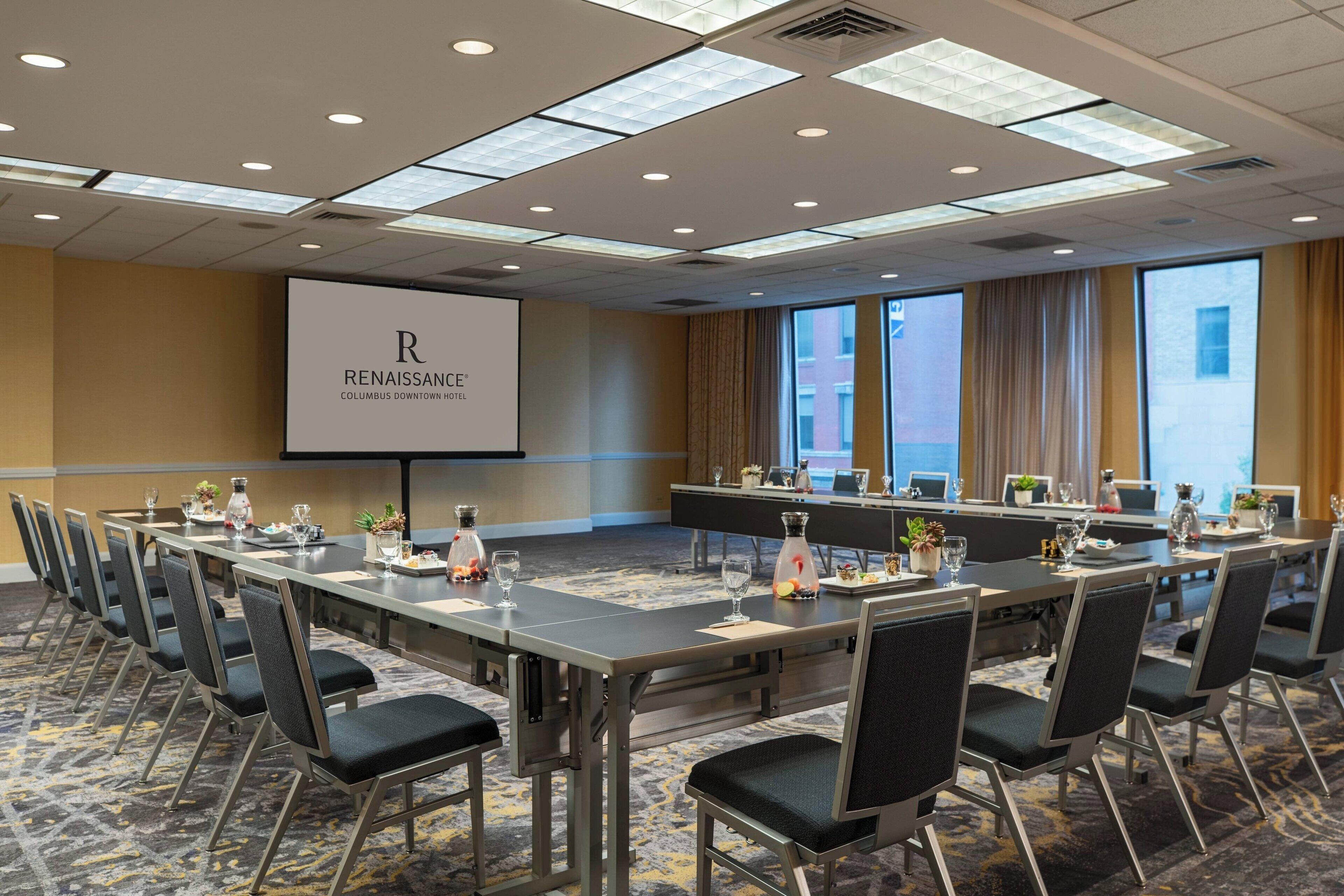 A conference room with a large table, chairs, a projector screen, and a view of the city.
