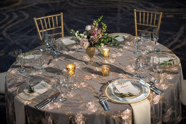 A round dining table set for a formal event with gold accents, floral centerpieces, and candle holders.