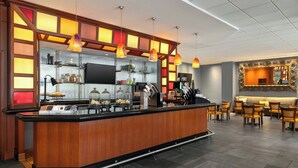 A modern bar area with a wooden counter, pendant lighting, and a seating area with chairs and a sofa. - Renaissance Columbus Downtown Hotel (Columbus)