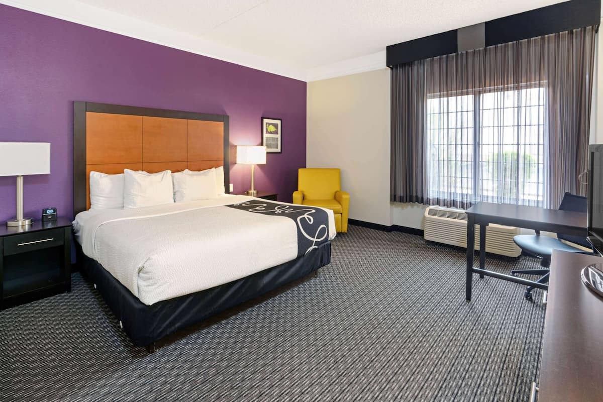 Een hotelkamer met een groot bed, een bureau, een stoel, een televisie, een lamp en een raam met gordijnen.