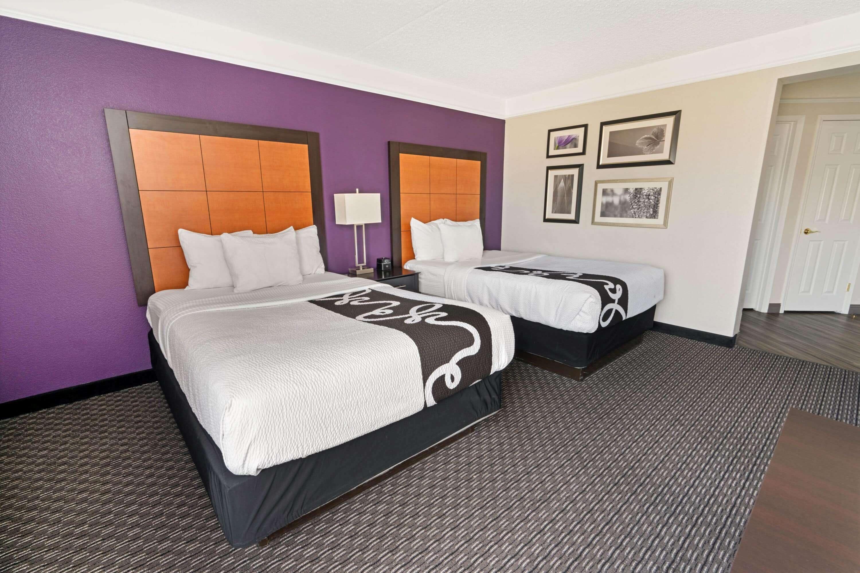 A hotel room with two beds, purple walls, and framed pictures on the wall.