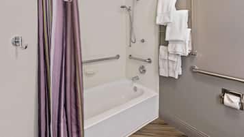 Une salle de bain avec une baignoire blanche, une douche avec un pommeau de douche amovible, un porte-serviettes avec plusieurs serviettes blanches et un porte-rouleau de papier toilette.