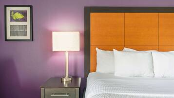 Habitación de hotel con cama, mesita de noche con lámpara, un cuadro en la pared y pared morada.