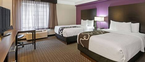 A hotel room with two beds, a desk, a chair, a TV, and a window with curtains.