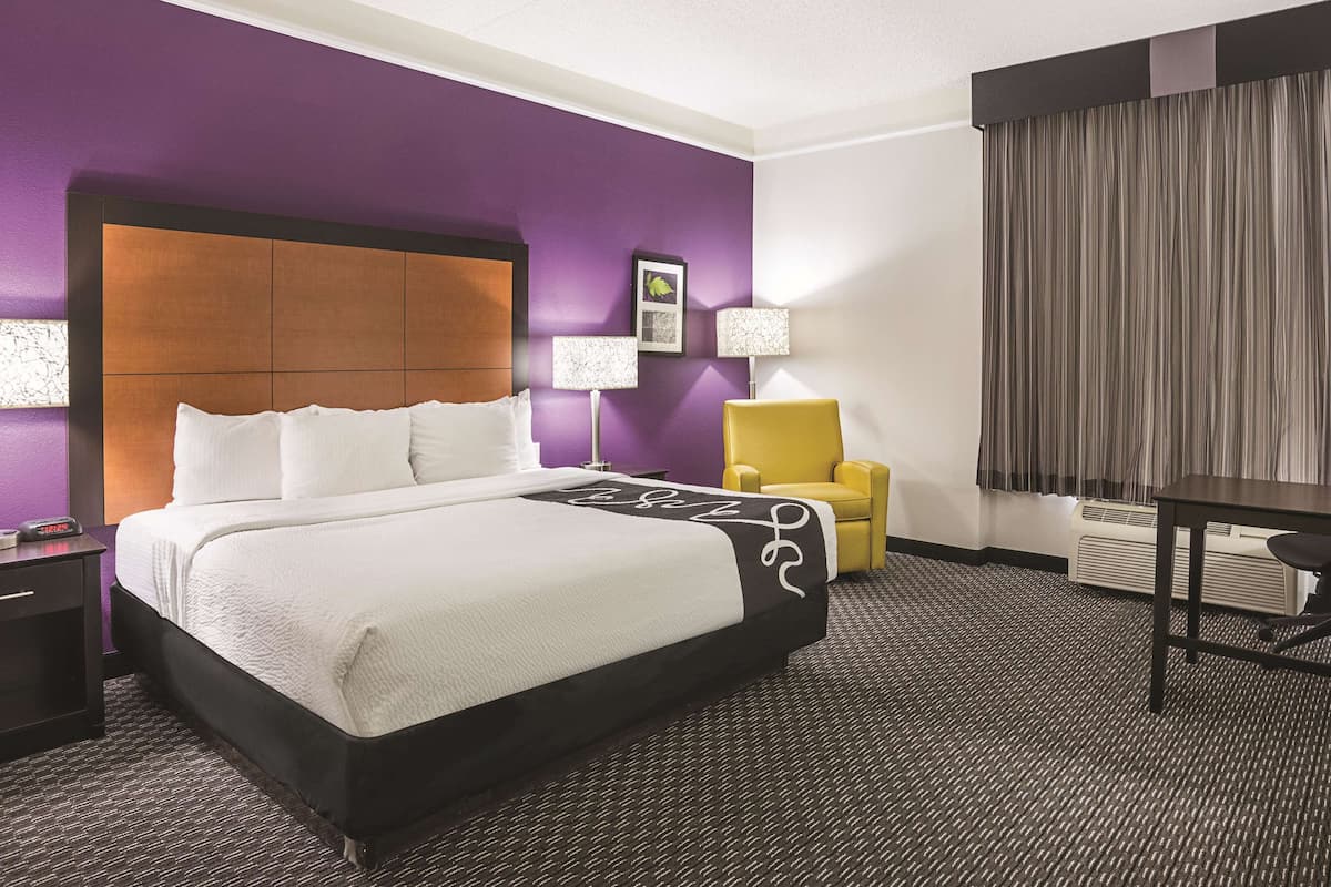 Een hotelkamer met een groot bed, een nachtkastje, een stoel, een bureau en een raam met gordijnen.