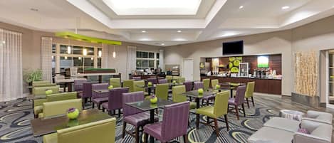 A hotel lobby with multiple seating areas, a reception desk, and a kitchen in the background.