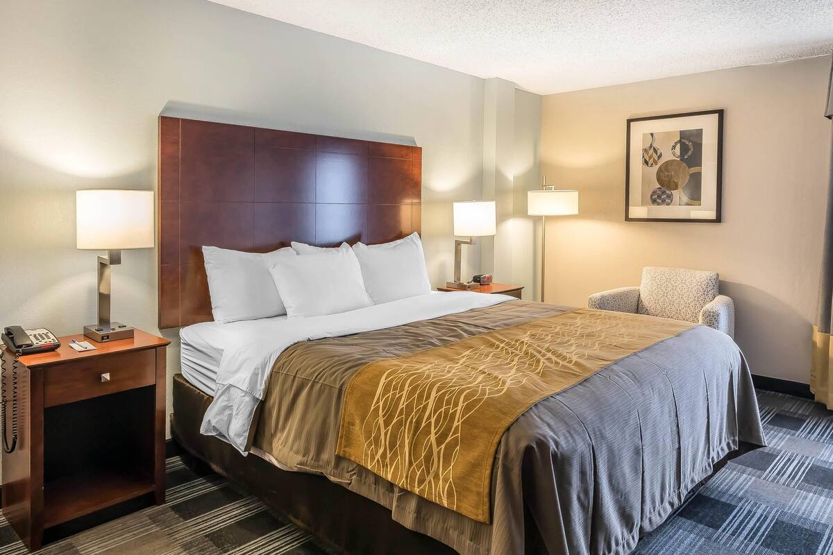 A hotel room with a large bed, two bedside tables with lamps, a chair, and a framed picture on the wall.