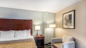 A hotel room with a large bed, a small desk with a lamp, a chair, and a framed picture on the wall.