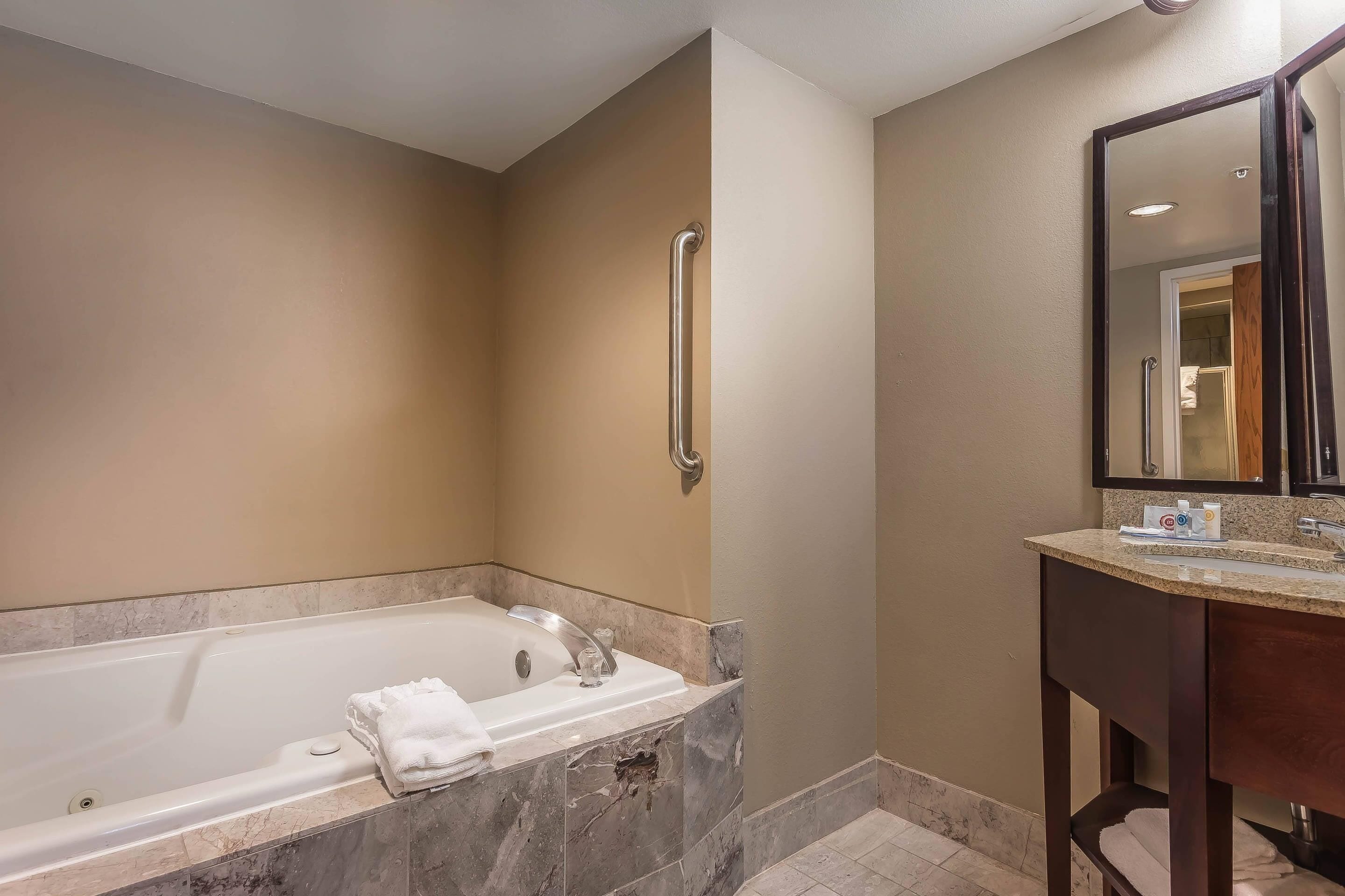 A bathroom with a bathtub, a sink, a mirror, and a handrail.