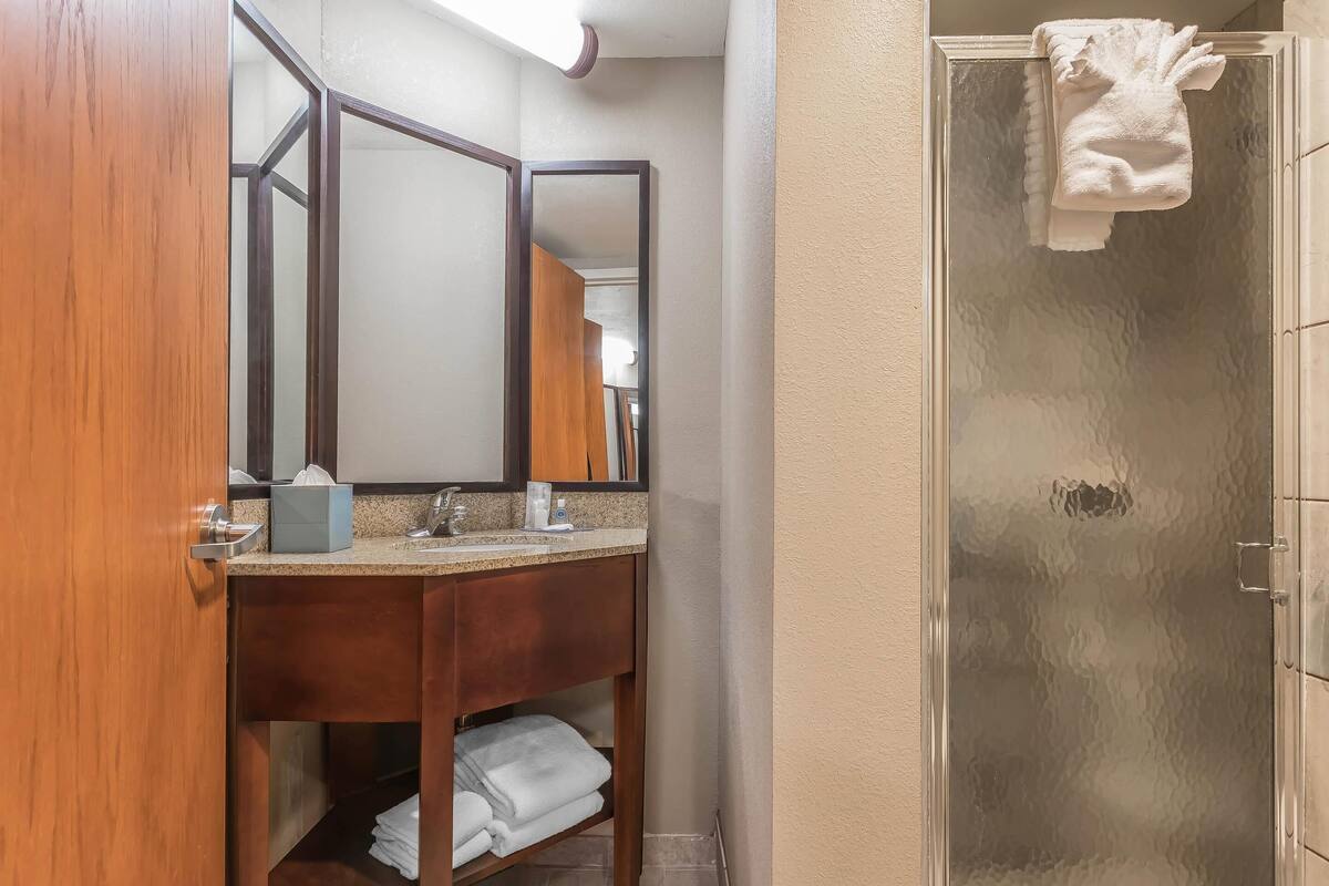 A bathroom with a wooden vanity, a mirror, a sink, and a glass shower enclosure.
