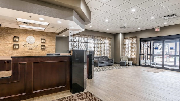 A hotel reception area with a wooden reception desk, a large wall clock, and a patterned curtain.