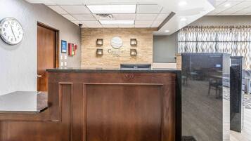 A hotel reception desk with a clock, a wooden reception area, and a wall-mounted sign.