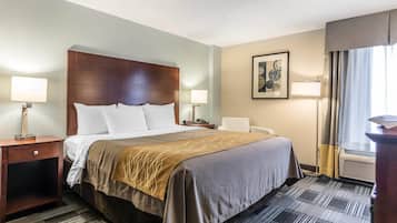 A hotel room with a large bed, two bedside tables with lamps, a chair, a framed artwork on the wall, and a window with curtains.