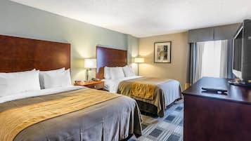 A hotel room with two beds, a desk, a TV, and a window with curtains.