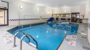 An indoor swimming pool with clear lane markings, a safety ladder, and a seating area with chairs and a table.