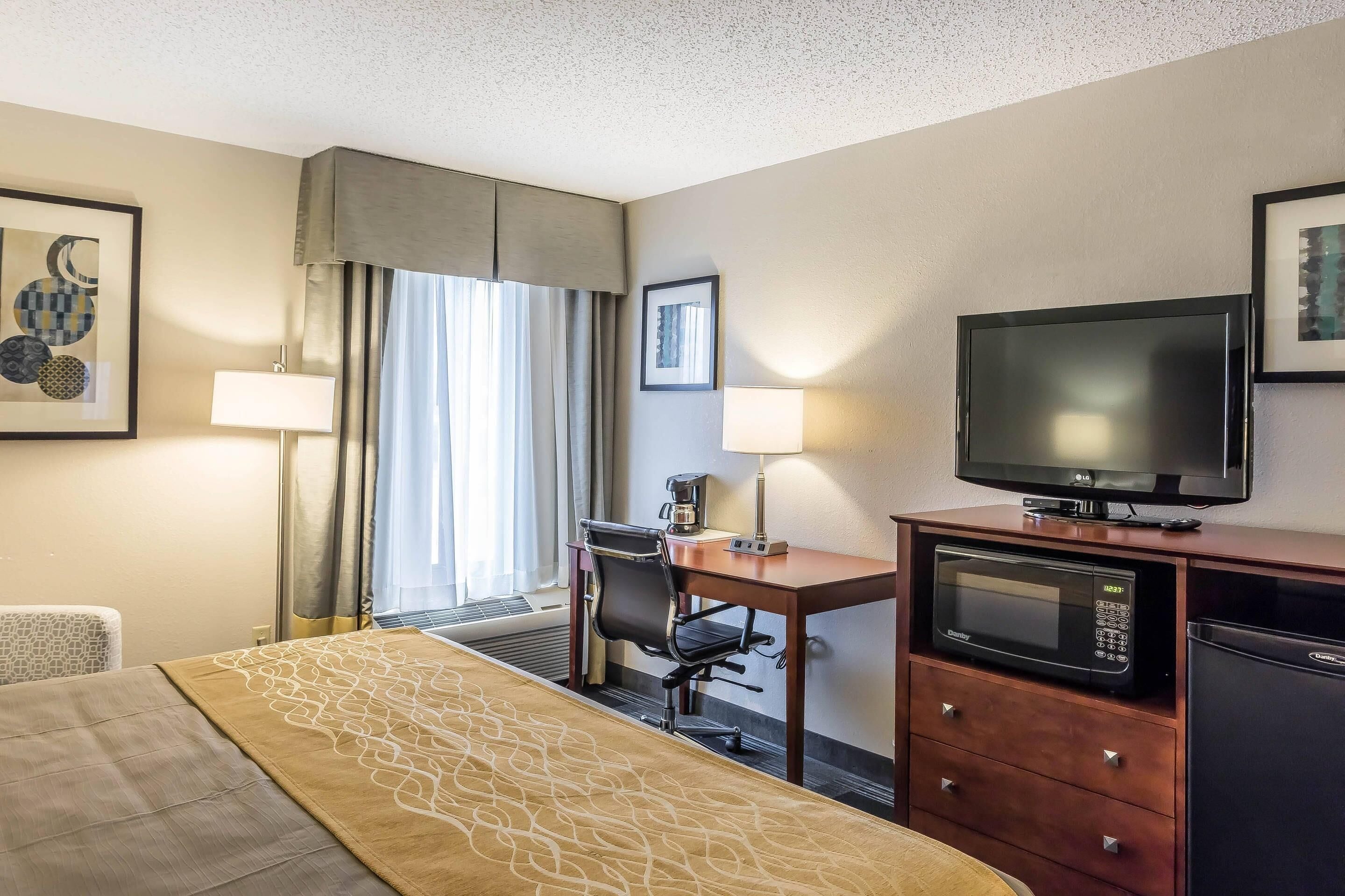 A hotel room with a bed, desk, chair, television, microwave, and refrigerator.