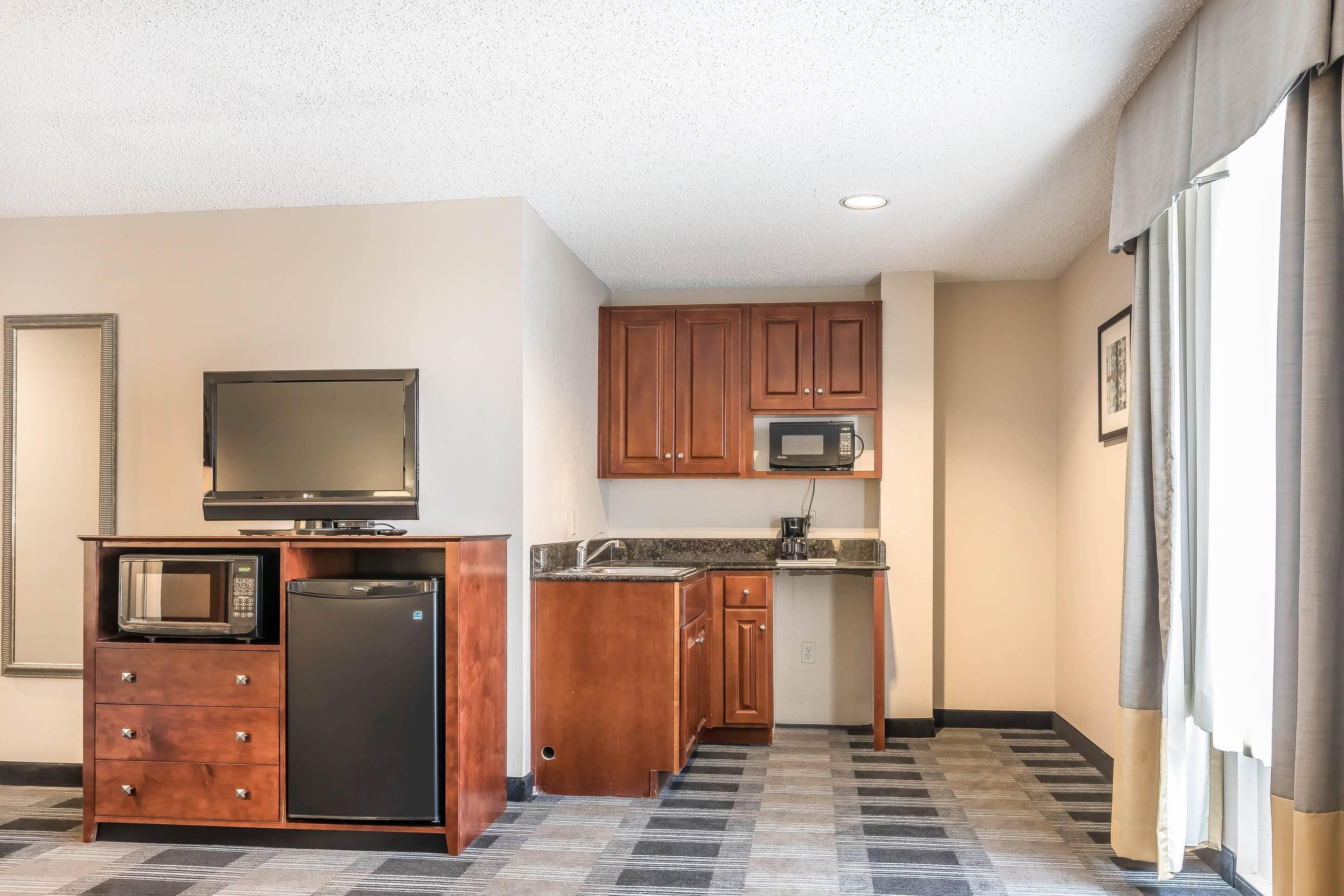 A compact kitchen with wooden cabinets, a microwave, a refrigerator, and a television on a wooden cabinet.