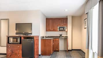 A compact kitchen with wooden cabinets, a microwave, a refrigerator, and a television on a wooden cabinet.