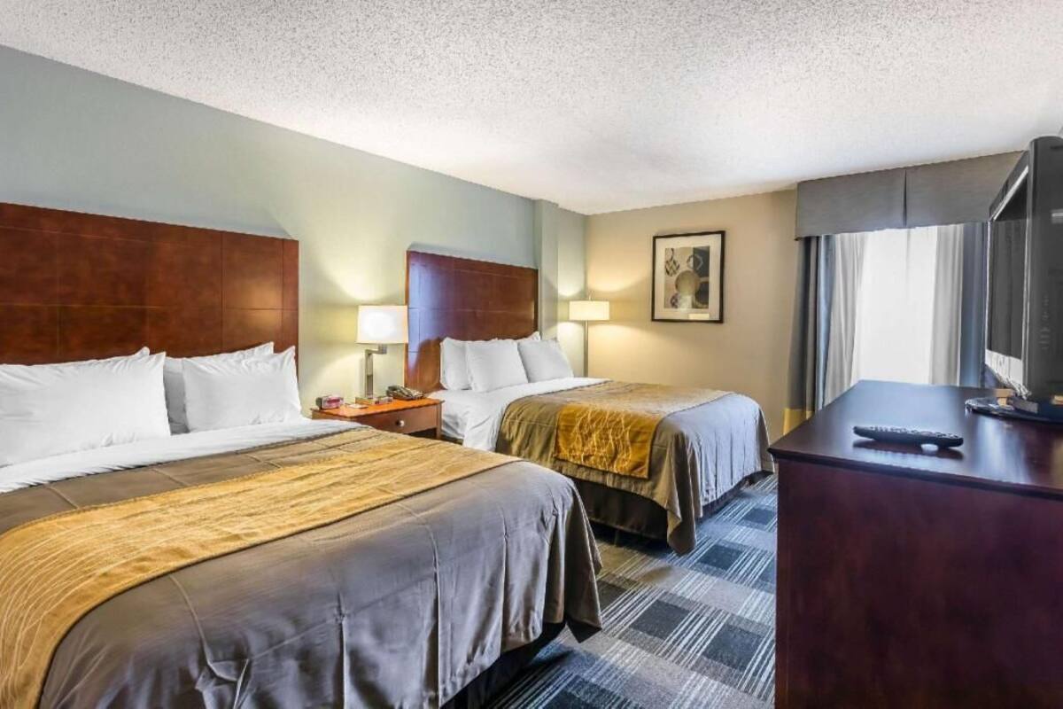 A hotel room with two beds, a desk with a TV, and a window with curtains.