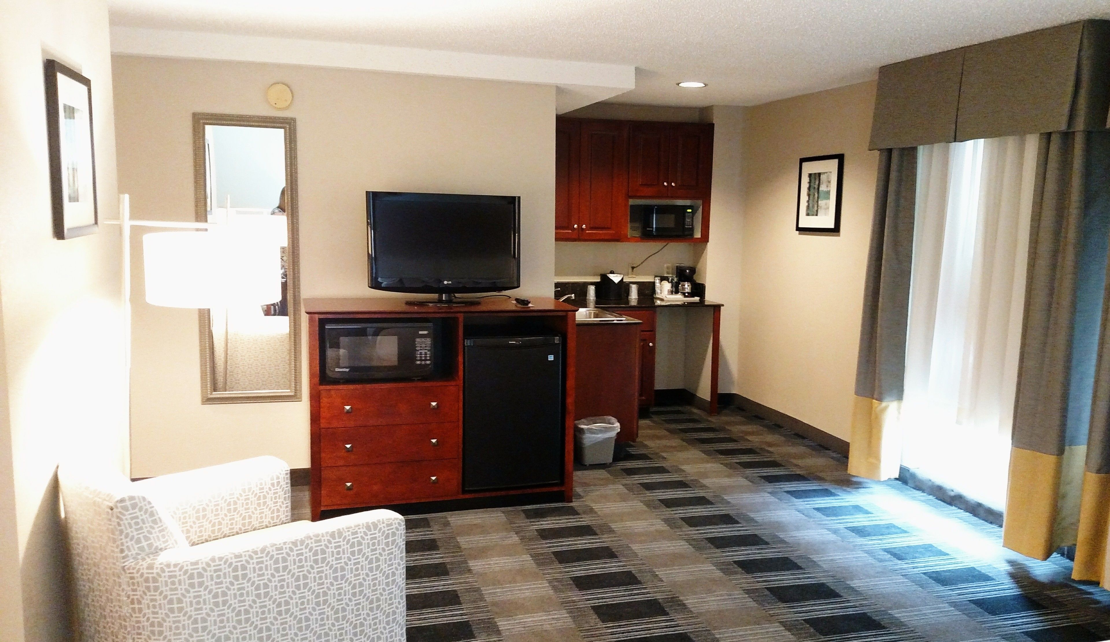 A compact hotel room with a kitchenette, a television, a small refrigerator, a microwave, a sink, and a trash bin.