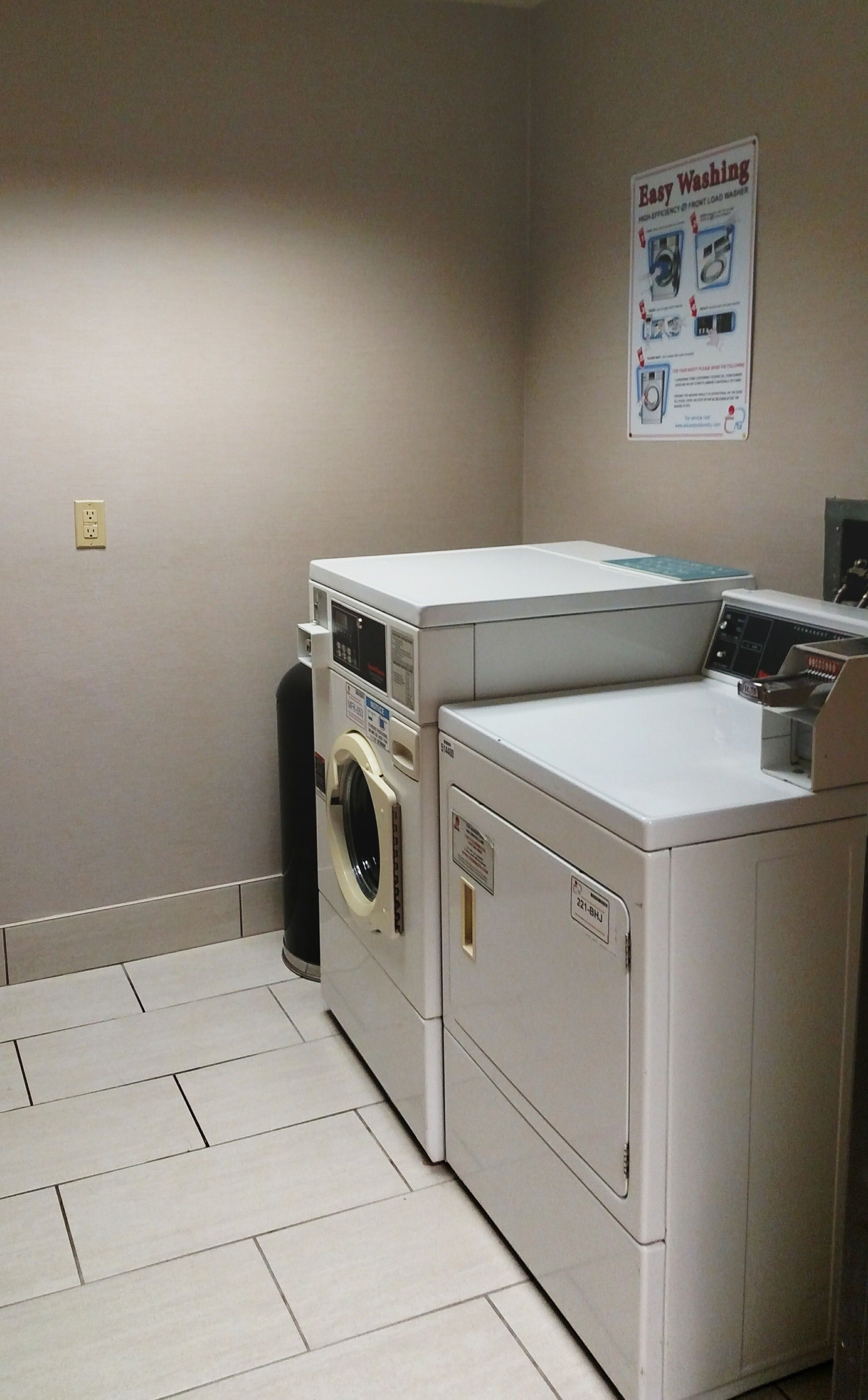 A laundry room with two washing machines and a dryer, a poster on the wall, and a tiled floor.