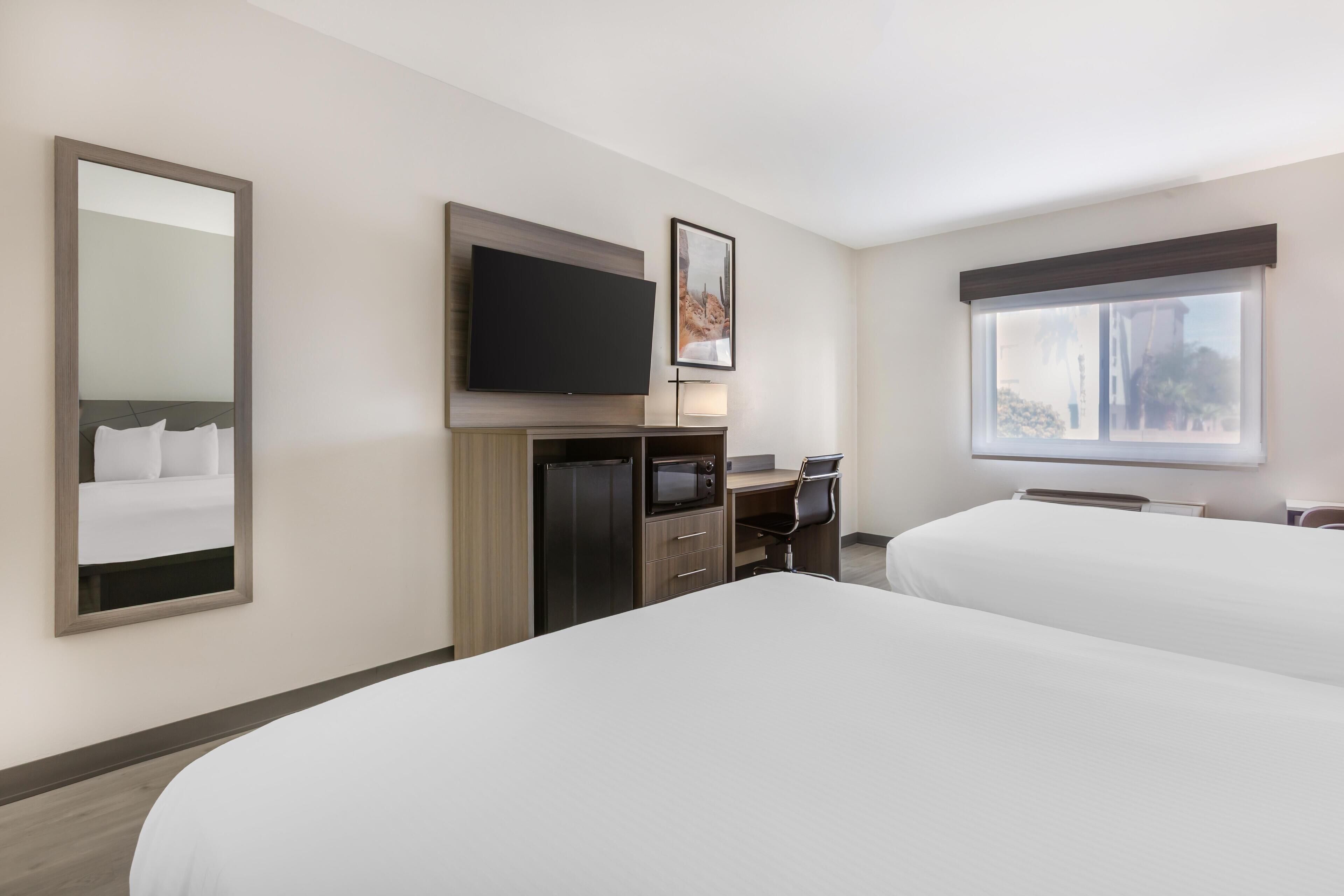 A hotel room with two beds, a desk, a flat-screen TV, a microwave, and a large window.