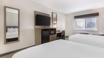 A hotel room with two beds, a desk, a flat-screen TV, a microwave, and a large window.