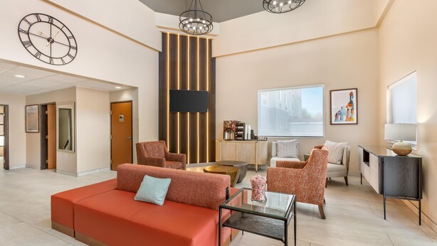 Un hall d’hôtel moderne avec un canapé rouge, plusieurs fauteuils, une table basse en verre, un téléviseur fixé au mur et une grande fenêtre donnant sur le paysage urbain.