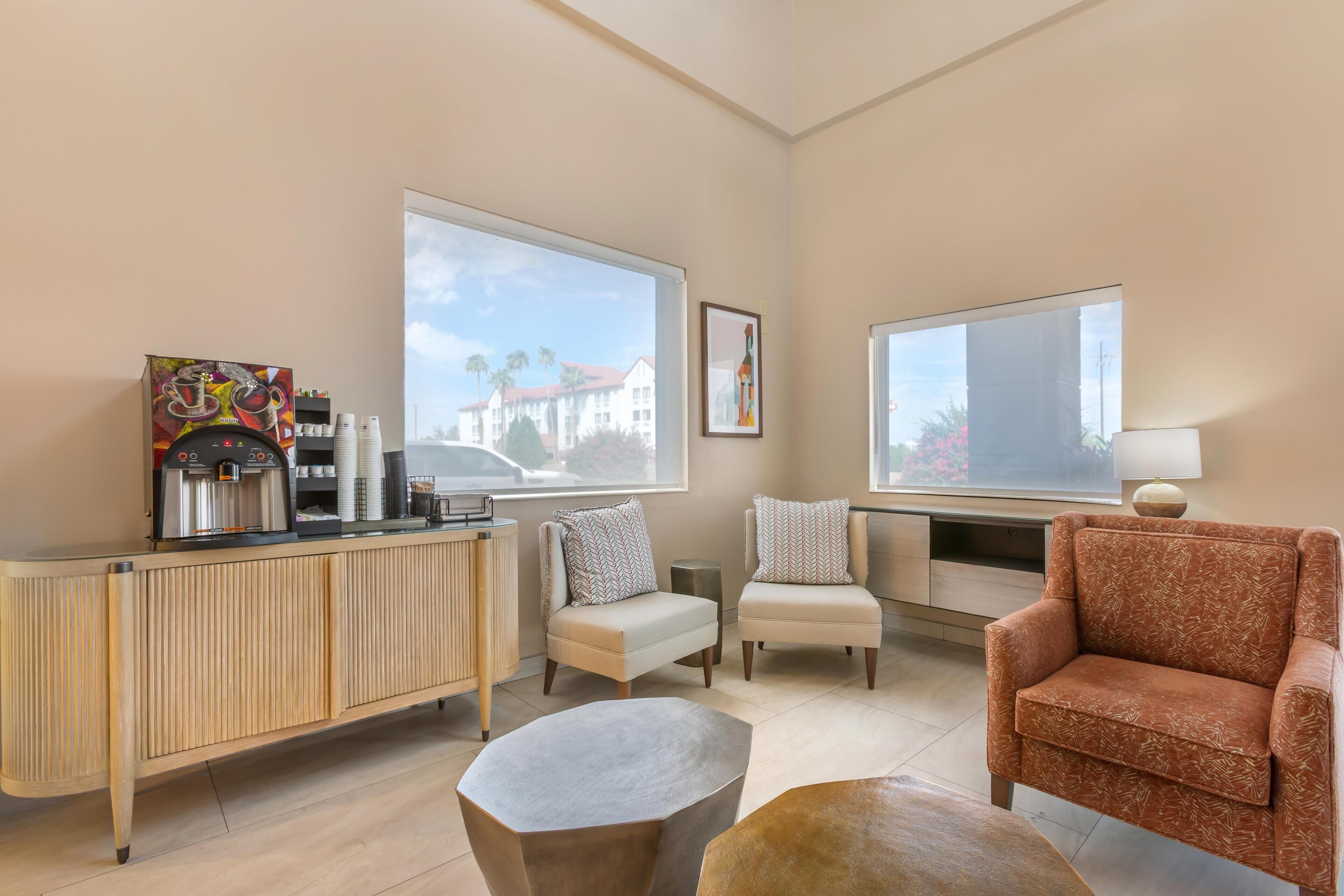 A modern living room with a wooden console table, two armchairs, a sofa, and a coffee machine.