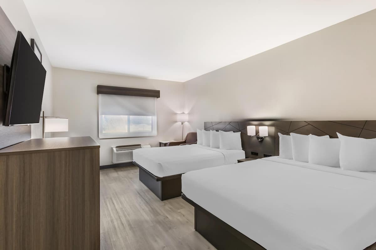Une chambre d’hôtel avec deux lits, un bureau, une télévision, une fenêtre et une lampe fixée au mur.