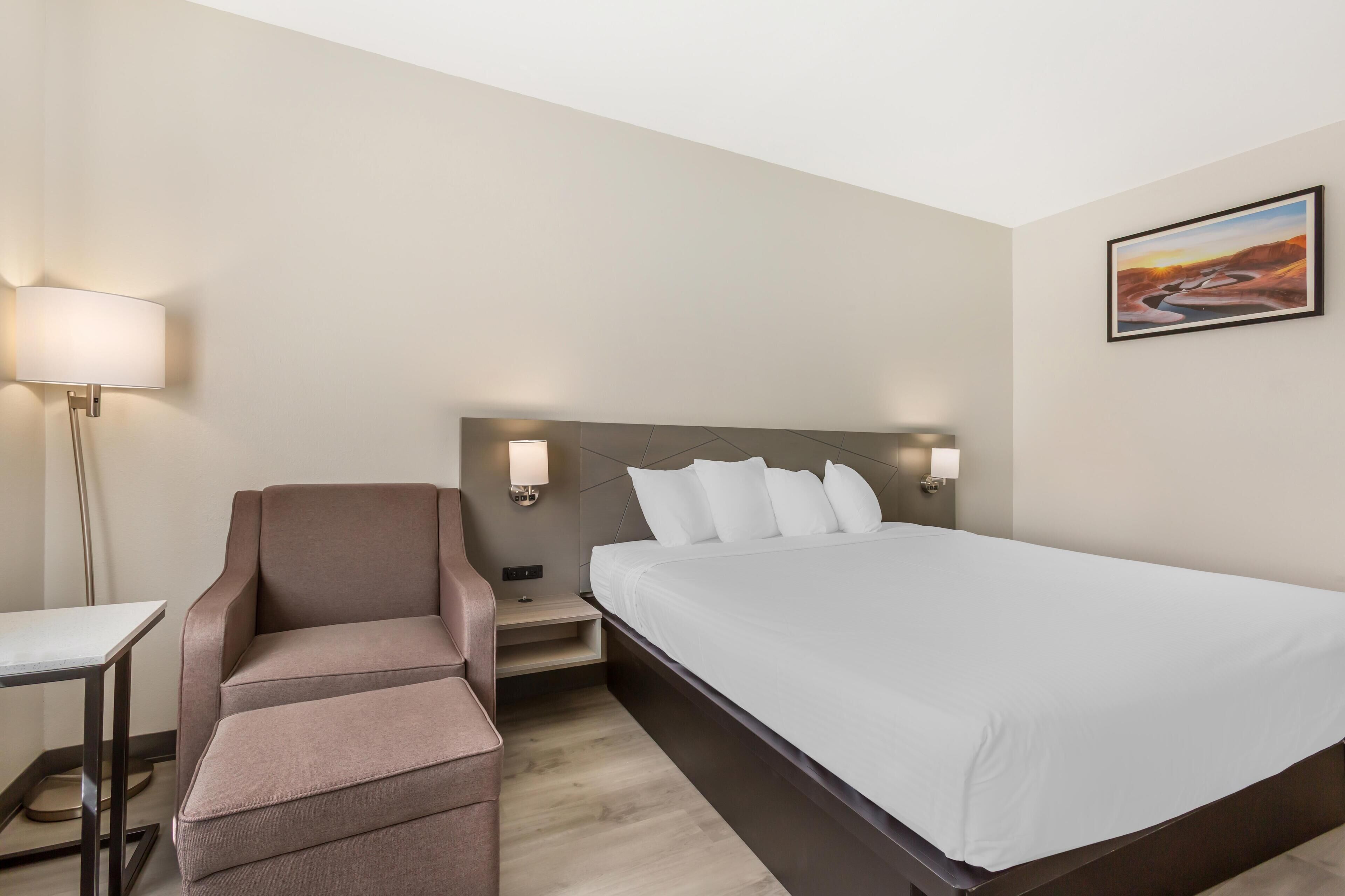 A hotel room with a bed, a desk, a chair, and a nightstand.