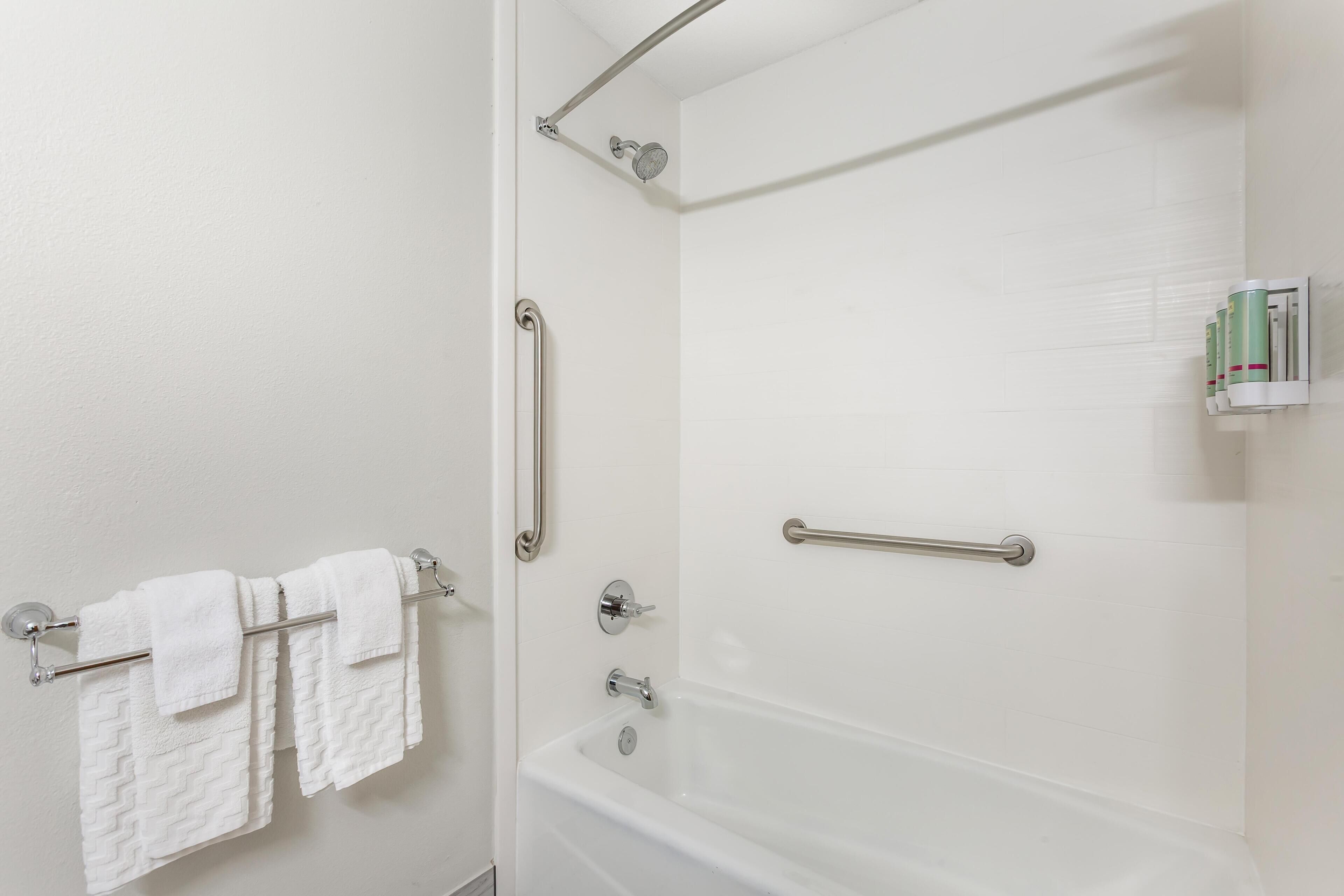 Un baño con bañera, barras de apoyo y un perchero con toallas blancas.