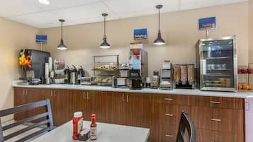 A self-service breakfast area with a coffee machine, toaster, and refrigerated display case.