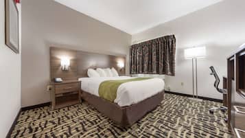 A hotel room with a large bed, bedside table, lamp, and patterned carpet.