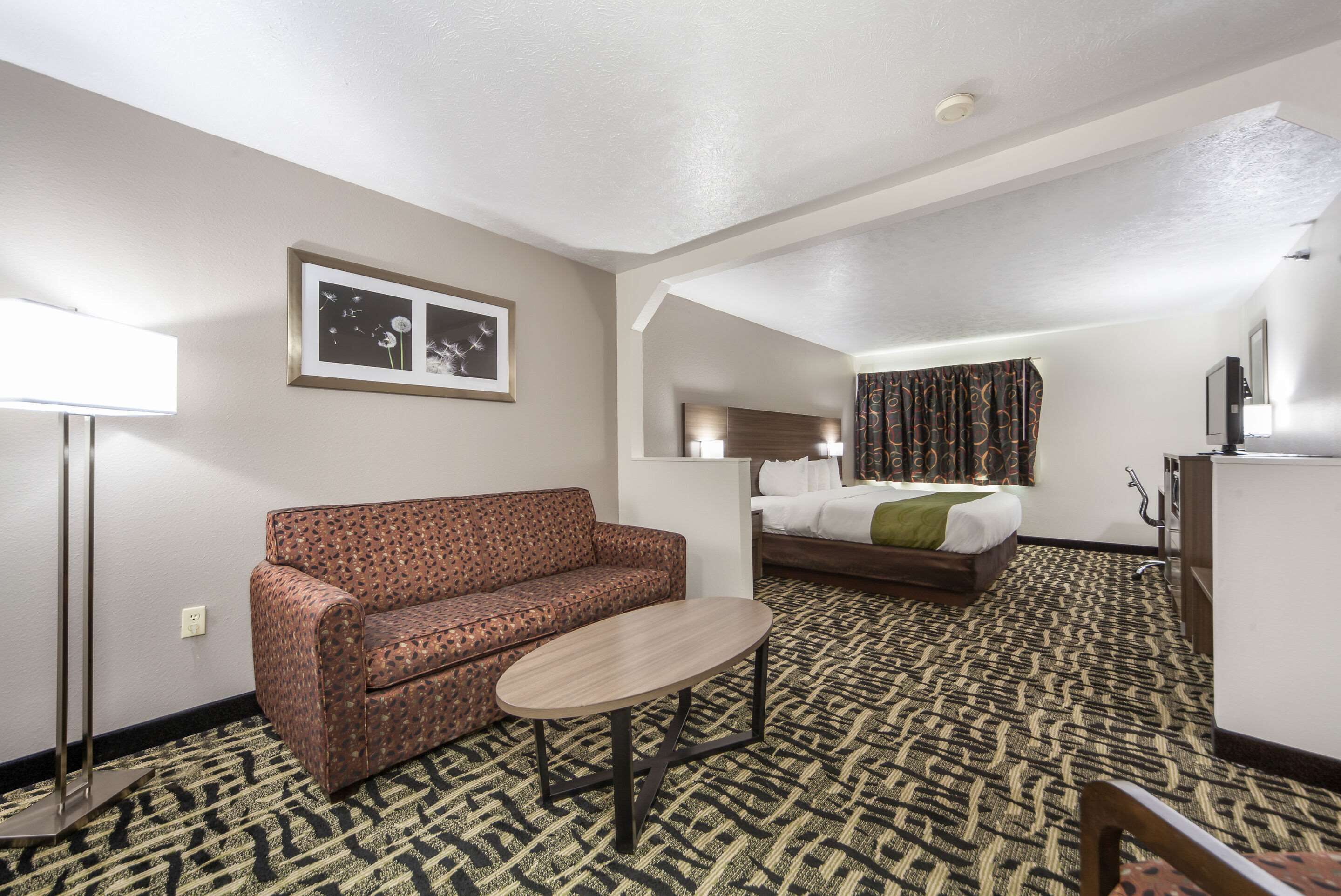 Habitación de hotel con sofá, una mesita, cama, cómoda y un cuadro en la pared.