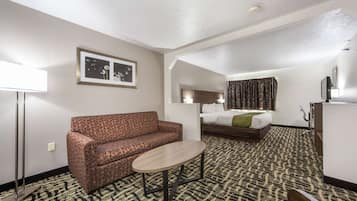 A hotel room with a sofa, a small table, a bed, a dresser, and a framed picture on the wall.