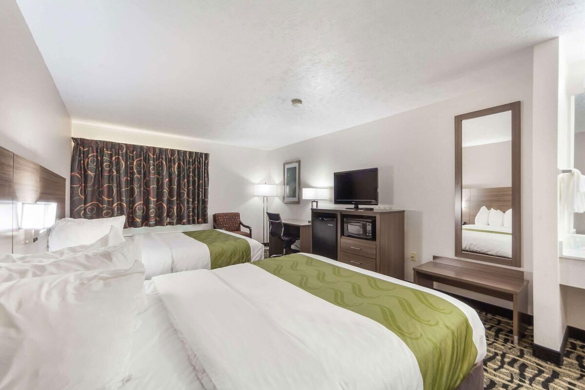 Habitación de hotel con dos camas, un escritorio, un televisor, un microondas y un espejo.