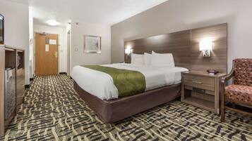 A hotel room with a large bed, a wooden nightstand, a chair, and a patterned carpet.