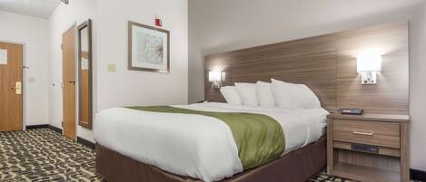 A hotel room with a large bed, a wooden headboard, a nightstand, and a patterned carpet.