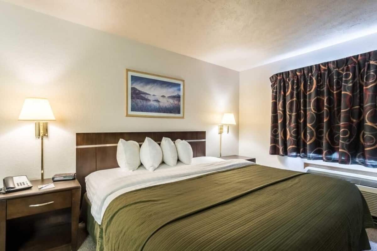 A hotel room with a bed, two bedside lamps, a painting on the wall, and a window with curtains.