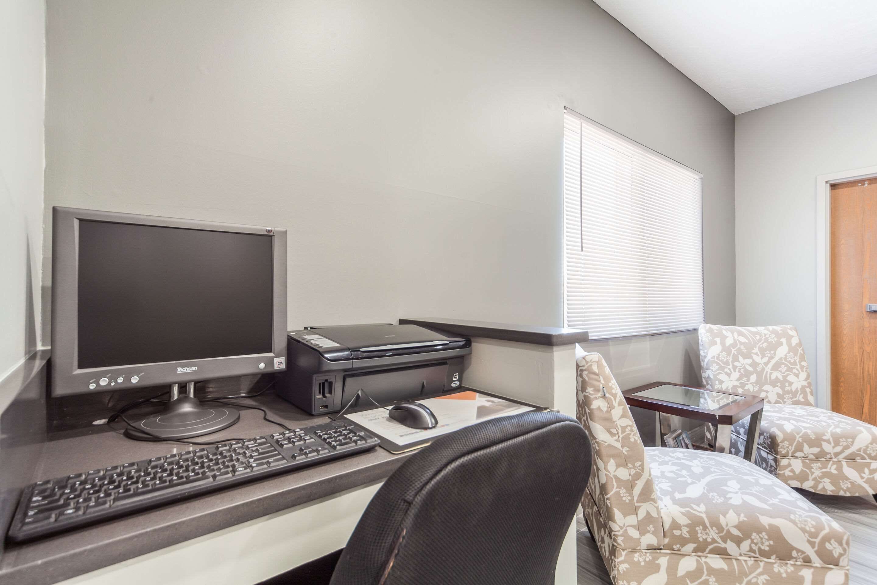 A home office setup with a desktop computer, printer, and two patterned chairs.