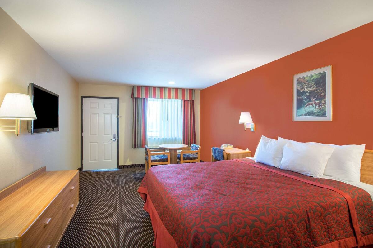 A hotel room with a bed, a desk, a chair, a television, and a door.