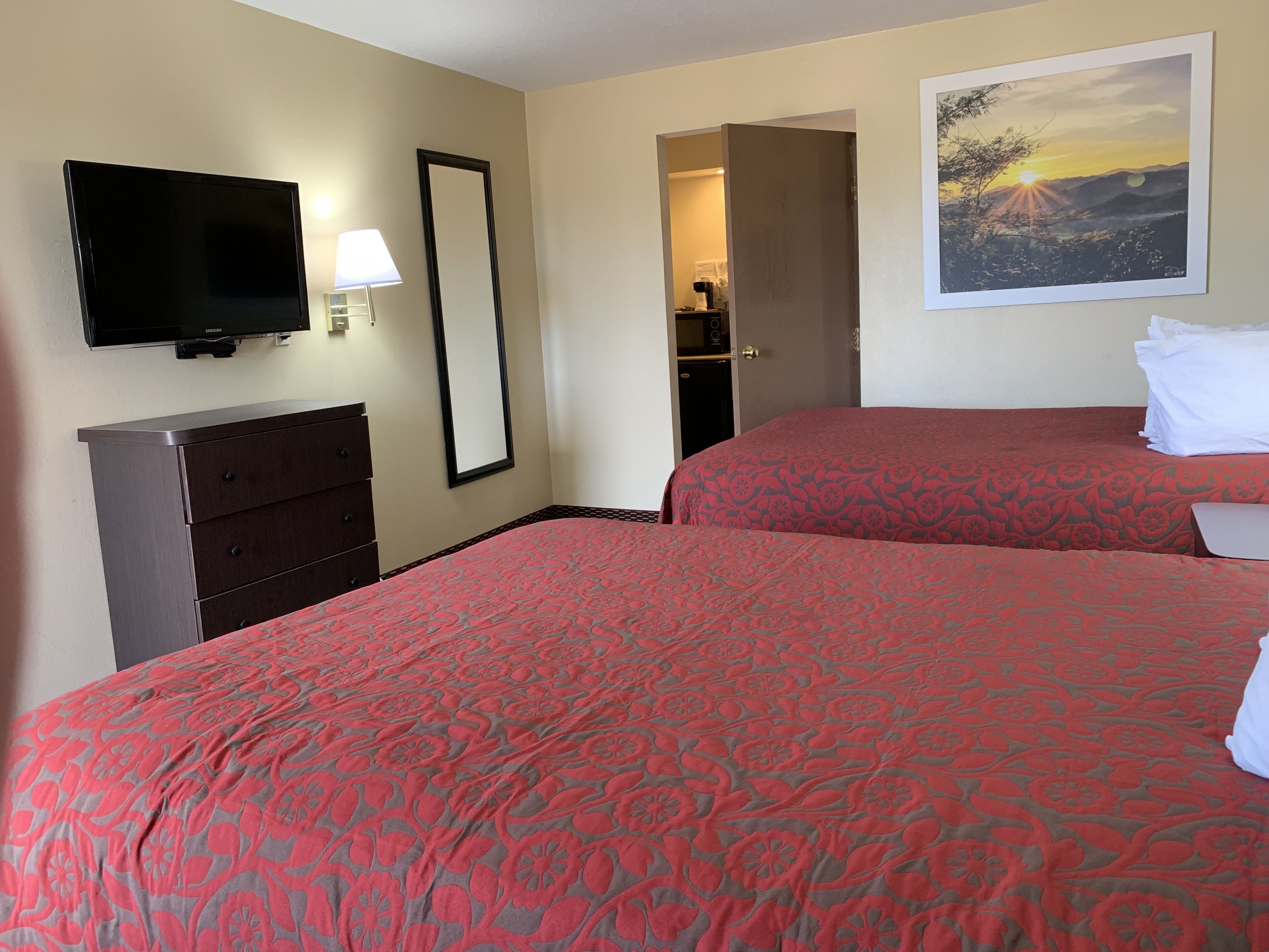 Une chambre d’hôtel avec deux lits, une télévision, une commode et un tableau au mur.