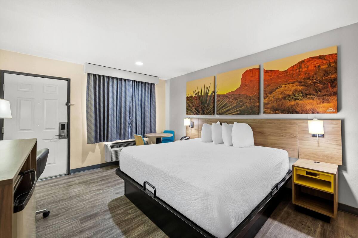 A hotel room with a large bed, a desk, a chair, a nightstand, and a wall-mounted lamp.