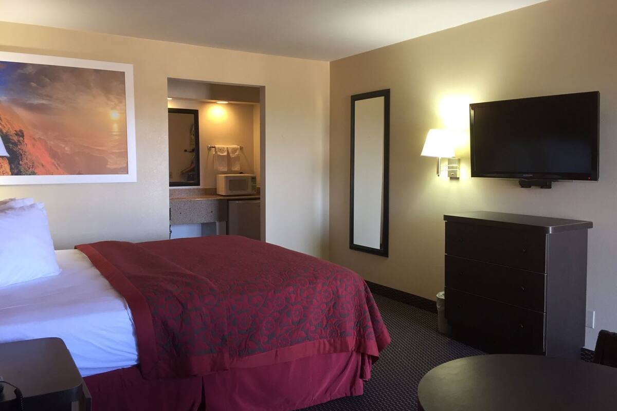A hotel room with a bed, a television, a desk, a mirror, and a painting on the wall.