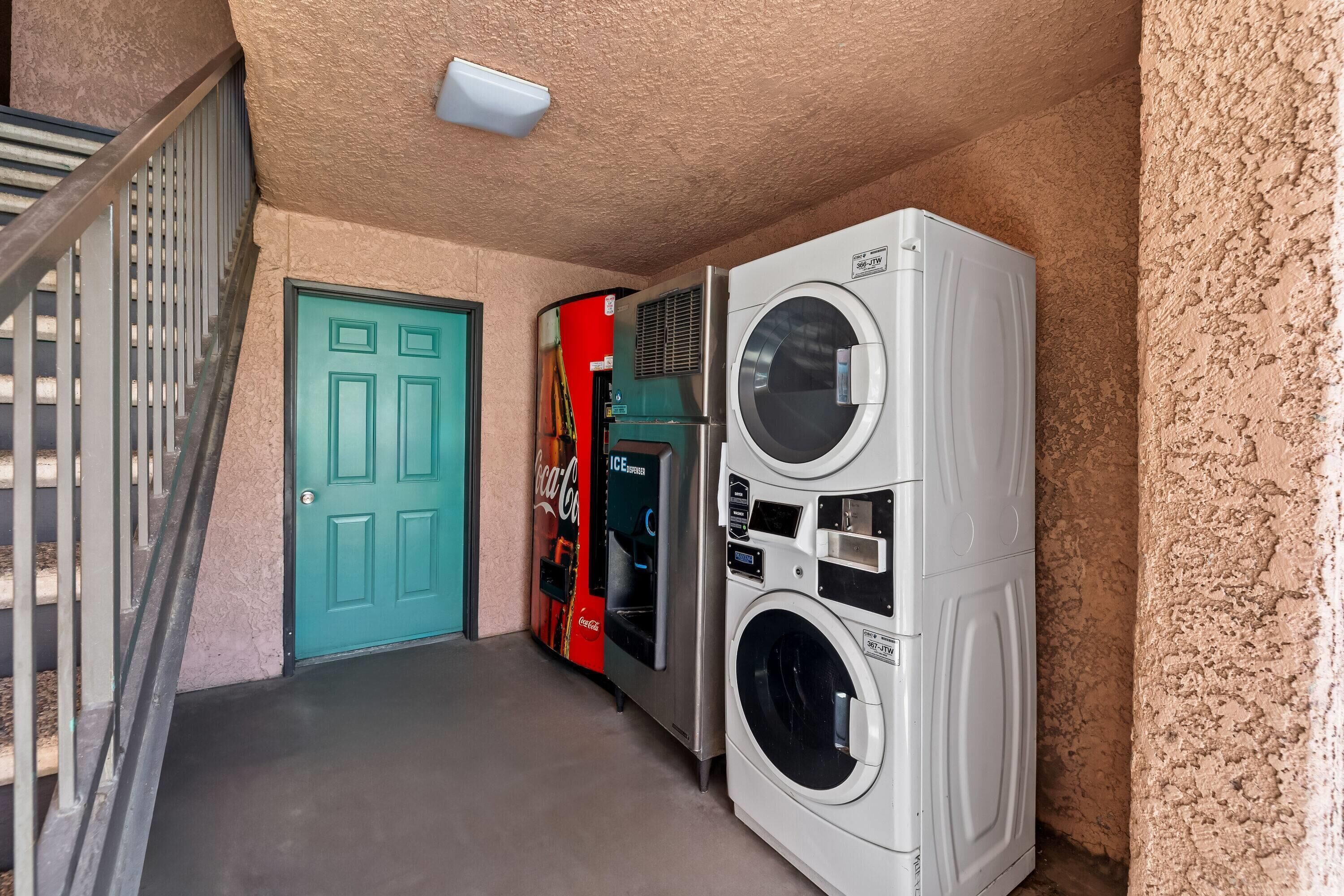 A laundry area with two washers and dryers, a Coca-Cola vending machine, and a teal door.